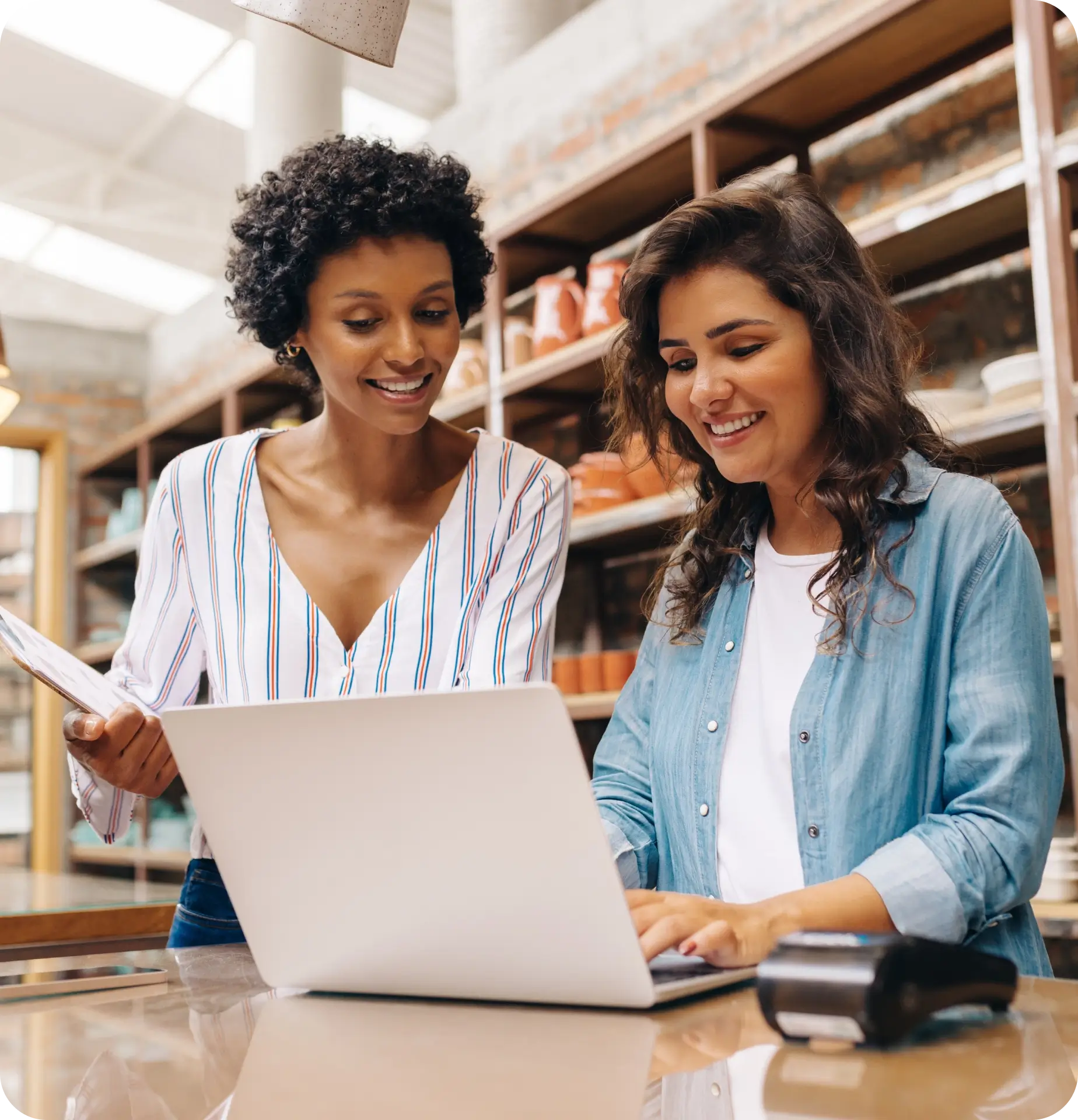 Two women smile while looking at a laptop on a counter.